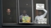 FILE - Three asylum seekers look out at protesters rallying outside in their support, from their hotel room where they have been detained in Melbourne, Australia, June 13, 2020.