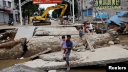 FILE - A man holding a child walks across a damaged bridge after rains and floods brought by remnants of Typhoon Doksuri, in Zhuozhou, Hebei province, China August 7, 2023. (REUTERS/Tingshu Wang)