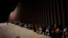 FILE - Migrants wait along a border wall Aug. 23, 2022, after crossing from Mexico near Yuma, Ariz.