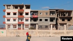 Seorang perempuan berjalan membawa bayinya melewati gedung sekolah yang dijadikan tempat penampungan sementara bagi para korban gempa Turki-Suriah di Jableh, Suriah, pada 16 Februari 2023. (Foto: Reuters/Amr Alfiky)