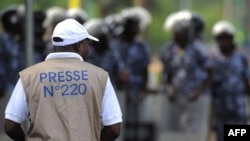 FILE - A reporter looks at security forces preventing a protest by journalists and members of the public in front of the Palais des Congres in Lome, Togo, Feb. 19, 2013. Two journalists in Togo were sentenced to three years this week for insulting public authorities.