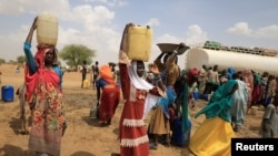 Sudanese refugee women who fled violence in Sudan's Darfur region carry jerrycans of water as they walk to their shelter near the border between Sudan and Chad in Koufroun, Chad, May 10, 2023.