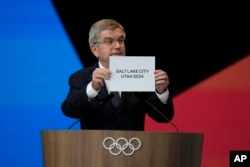 Presiden IOC Thomas Bach memegang papan nama "Salt Lake City, Utah" saat mengumumkan tuan rumah yang terpilih untuk penyelenggaraan Olimpiade Musim Dingin 2034. (Natacha Pisarenko/AP)
