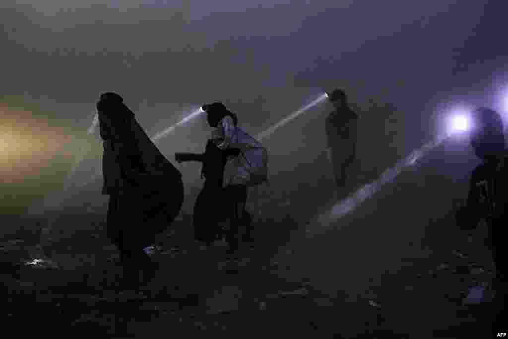 People equipped with searchlights scan for recyclable materials for resale at a landfill in Iraq's southern city of Basra late at night, June 22, 2023.
