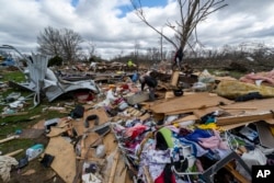 FILE - People walk through damage from a late-night tornado in Sullivan, Ind., April 1, 2023. (AP Photo/Doug McSchooler, File)