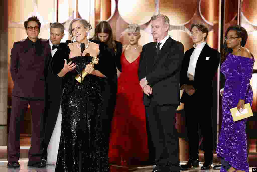 This image released by CBS shows producer Emma Thomas, foreground left, accepting the award for best motion picture drama for "Oppenheimer" as cast and crew members, background from left, Robert Downey Jr., Matt Damon, composer Ludwig Göransson, Florence Pugh, director Christopher Nolan, actor Cillian Murphy and presenter Oprah Winfrey look on during the 81st Annual Golden Globe Awards.