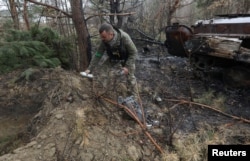 Seorang personel mengambil bagian dari bom klaster yang tidak meledak setelah invasi Rusia dekat desa Motyzhyn, wilayah Kyiv, Ukraina, 10 April 2022. (Mykola Tymchenko/Reuters)
