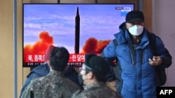 People watch a television screen showing a news broadcast with file footage of a North Korean missile test, at a railway station in Seoul on Feb. 27, 2022. 