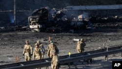 Soldados ucranianos passam por destroços de um camião militar em chamas numa rua em Kyiv, Ucrânia, 26 de Fev. 2022. Tropas russas invadiram a capital da Ucrânia no sábado, e os combates de rua eclodiram.