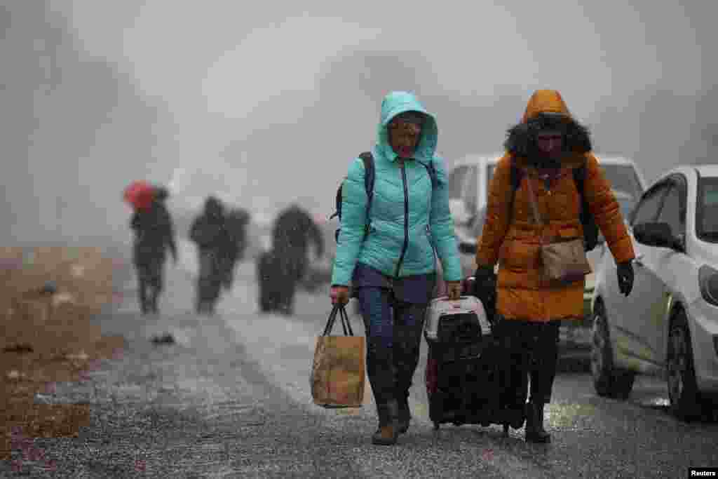 People fleeing Russia&#39;s military operation against Ukraine walk toward the Shehyni border crossing to Poland past cars waiting in line to cross the border, outside Mostyska, Ukraine.