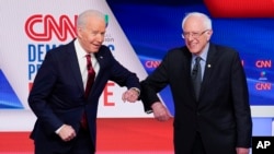 El exvicepresidente Joe Biden y el senador Bernie Sanders se saludan con un contacto de brazos, como medida de protección al coronavirus, antes de iniciar su primer debate personal el 15 de marzo de 2020.