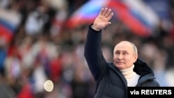 Presiden Rusia Vladimir Putin melambai saat konser menandai ulang tahun kedelapan pencaplokan Krimea oleh Rusia di Stadion Luzhniki di Moskow, Rusia, 18 Maret 2022. (Foto: Sputnik/Ramil Sitdikov/Kremlin via REUTERS)