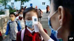 FILE - A teacher takes the body temperature of a schoolgirl to help curb the spread of the coronavirus before entering Kim Song Ju Primary School in Central District in Pyongyang, North Korea, on Oct. 13, 2021