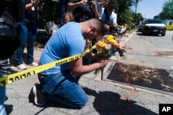 Joseph Avila, kiri, berdoa sambil memegang bunga untuk menghormati para korban yang tewas dalam penembakan Selasa di Sekolah Dasar Robb di Uvalde, Texas, 25 Mei 2022. (Foto: AP)