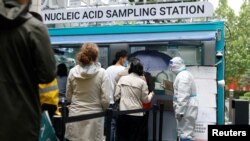Orang-orang berbaris untuk dites di sebelah anggota staf yang mengenakan APD di tempat pengujian asam nukleat seluler di luar pusat perbelanjaan, di tengah wabah COVID-19 di Beijing, China, 6 Mei 2022. (Foto: REUTERS/Carlos Garcia Rawlins)