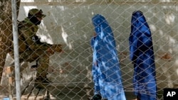 Seorang anggota Taliban berjaga-jaga ketika dua perempuan memasuki kantor paspor pemerintah, di Kabul, Afghanistan, 27 April 2022. (Foto: AP)