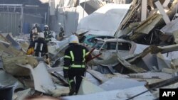 Rescue workers walk past debris and cars under ruins in front of the shopping and entertainment center in the Ukrainian Black Sea city of Odessa on May 10, 2022, destroyed after Russian missiles strike late on May 9, 2022.