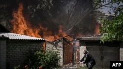 Mwanamke akiondoka katika nyumba inayoungua moto baada ya kupigwa bomu na wanajeshi wa Russia katika mji wa Lysytsansk mashariki mwa Ukrain. May 30, 2022