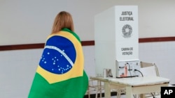 Yon elekte vlope ko li ak drapo Brezilyen an nan moman li rive nan biwo d vot pou depoze bilten li nan dezyem tou eleksyon prezidansyel la, Dimanch 30 Oktob, 2022. 