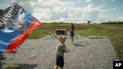 Seorang anak lelaki mengibarkan bendera Republik Rakyat Donetsk, sebuah negara yang diproklamasikan sendiri, di tempat dimana pesawat Malaysian Airlines MH17 ditembak jatuh di desa Hrabove, sebelah timur Ukraina, Kamis, 16 Juli 2015 (foto: AP Photo/Mstyslav Chernov)