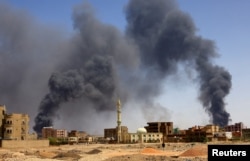 FILE - A man walks while smoke rises above buildings after aerial bombardment in Khartoum, Sudan, on May 1, 2023, two weeks after Sudan’s national army began fighting the rival Rapid Support Forces militia.