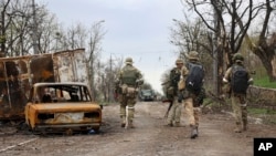 Militares de la milicia de la República Popular de Donetsk pasan junto a vehículos dañados durante un intenso combate en un área controlada por las fuerzas separatistas respaldadas por Rusia en Mariupol, Ucrania, el 19 de abril de 2022.