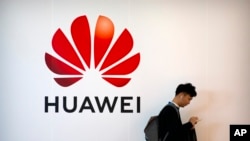 FILE - A man uses a smartphone near a billboard for Chinese tech firm Huawei at the PT Expo in Beijing, Oct. 31, 2019. U.S. President Joe Biden on June 3, 2021, barred U.S. investors from financial interests in Huawei and 58 other Chinese companies.