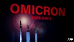 This photograph taken on December 1, 2021 shows syringes and a screen displaying Omicron, the name of the new covid 19 variant in Toulouse, southwestern France. 