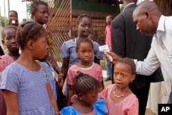 A health care worker, right, takes youngsters' temperatures for signs of the Ebola virus before they enter school in Conakry, Guinea, Jan. 19, 2015.