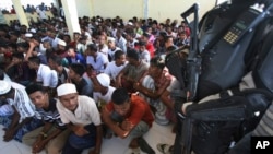 A police officer stands guard as ethnic Rohingya men gather upon arrival at a temporary shelter in Lhoksukon, Indonesia, for migrants whose boats were washed ashore earlier on Sumatra island, May 13, 2015.