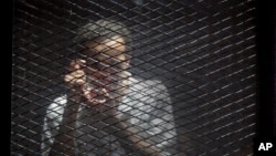 FILE - Egyptian photojournalist Mahmoud Abu Zeid, known by his nickname Shawkan, gestures in a soundproof glass cage inside a makeshift courtroom in Tora prison in Cairo, Egypt, July 28, 2018. 