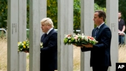 Britain's Prime Minister David Cameron, right, and London Mayor Boris Johnson walk through the 7/7 memorial in Hyde Park to lay wreaths in London, Tuesday, July 7, 2015.