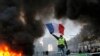A demonstrator waves the French flag onto a burning barricade on the Champs-Elysees avenue with the Arc de Triomphe in background, during a demonstration against the rising of the fuel taxes, Saturday, Nov. 24, 2018 in Paris.