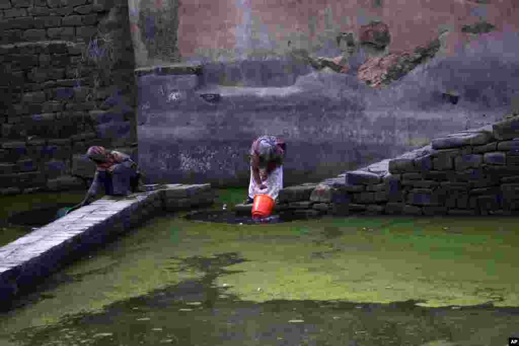 Dua orang perempuan mengambil air dari sebuah kolam air hujan di pinggiran kota Sana'a, Yaman.