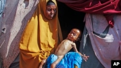 Boolo Aadan, 63, akiwa amembeba mjukuu wake wa umri wa miezi 9 katika kambi nje ya mji wa Mogadishu, Somalia, Feb. 4, 2022. 