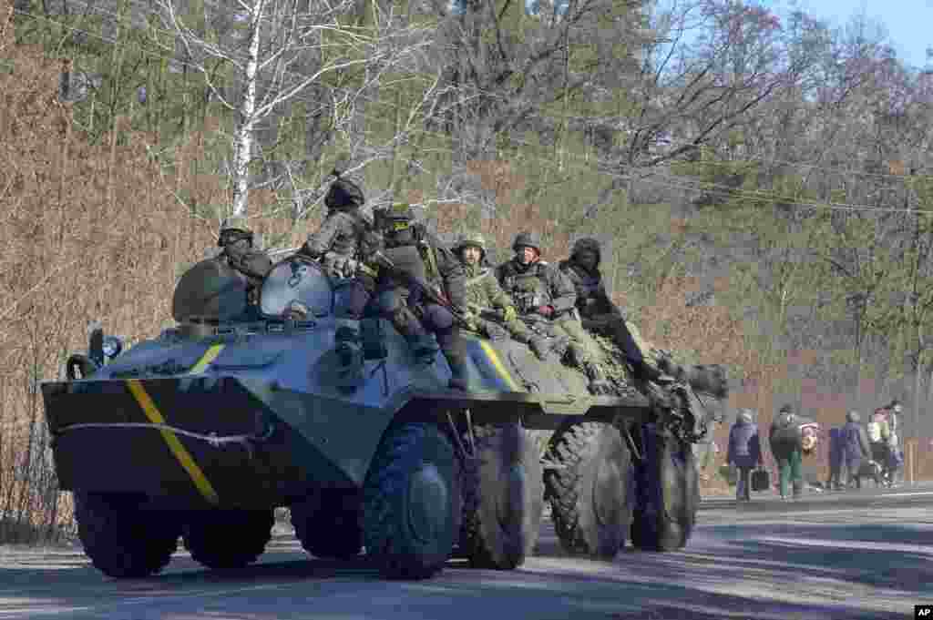 Ukrainian soldiers on an armored personnel carrier pass by people carrying their belongings as they flee the conflict, in the Vyshgorod region close to Kyiv, March 10, 2022. Russia’s two-week-long war in Ukraine has killed thousands of people and forced more than 2 million others to flee the country, shaking the foundations of European security.