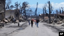 Unas personas caminan por una calle ante los daños causados por un incendio forestal, el viernes 11 de agosto de 2023, en Lahaina, Hawái.