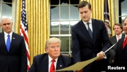 Le secrétaire du personnel de la Maison Blanche, Rob Porter, au centre, remet un document au président Donald Trump, à gauche, dans le bureau ovale de la Maison-Blanche, Washington, 20 janvier 2018.