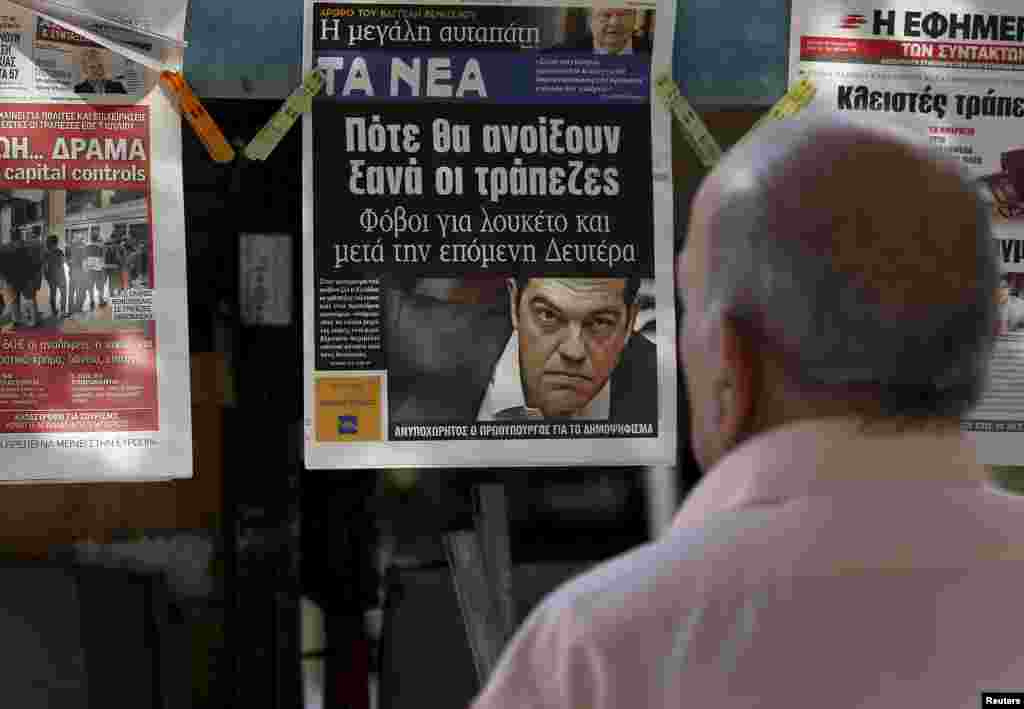 Seorang pria membaca halaman depan koran di sebuah kios di Athena (29/6). (Reuters/Yannis Behrakis)