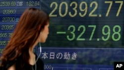 一位女士走过东京一家证券公司显示显示日经指数下跌的电子屏幕（2015年8月12日）