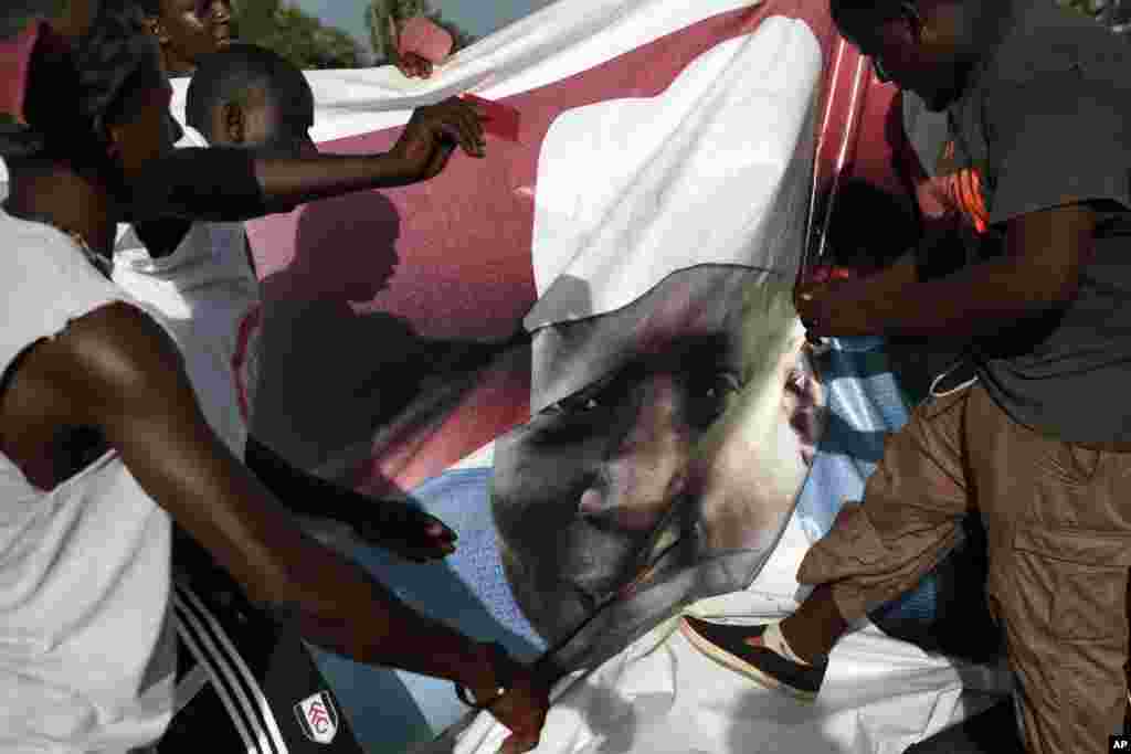 Warga merayakan kemenangan tokoh oposisi Adama Barrow dalam pilpres Gambia, dengan merobek poster bergambar Presiden Yahya Jammeh di jalanan kota Serrekunda, Gambia.