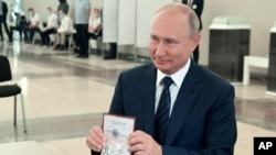 Presiden Rusia menunjukkan paspornya kepada petugas pemungutan suara saat tiba di tempat pemungutan suara di Moskow, Rusia, 1 Juli 2020.