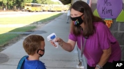 Asisten pengajar Crystal May berbicara dengan siswa taman kanak-kanak Lewis Henry Thompson, 5, saat dia mengukur suhu tubuhnya di Sekolah Dasar Newton County di Decatur, Mississippi, Senin, 3 Agustus 2020. (Foto: AP)