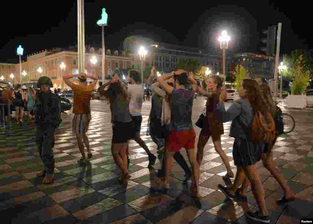 Warga menyeberang jalan dengan tangan di kepala setelah tentara Perancis mengamankan lokasi (15/7) tempat sebuah truk menabrak kerumunan massa di Promenade des Anglais di Nice, Perancis. (Reuters/Jean-Pierre Amet)