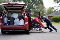 Lake Charles Fire Department personnel Alvin Taylor, right, and Jeremy Harris, left, assist Tim Williams into a transport van as he evacuates Lake Charles, La., Aug. 26, 2020, ahead of Hurricane Laura.