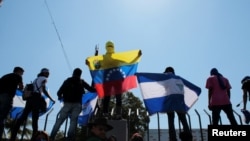 FILE - Anti-government protesters hold flags and shout slogans to riot police during a demonstration against Nicaraguan President Daniel Ortega's government in Managua, Nicaragua, March 30, 2019.