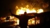 FILE - An opposition protester holds a machete in front of burning shops in Nairobi's Kibera slum, Dec. 30, 2007. Ten people have died in west Kenya as protests against Kibaki's controversial re-election erupted around the nation, the respected local…