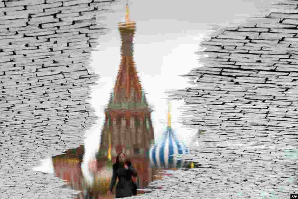 This photo, rotated 180 degrees, shows a woman reflected in a puddle as she walks past landmark St.Basil's Cathedral at the Red Square in Moscow, Russia.