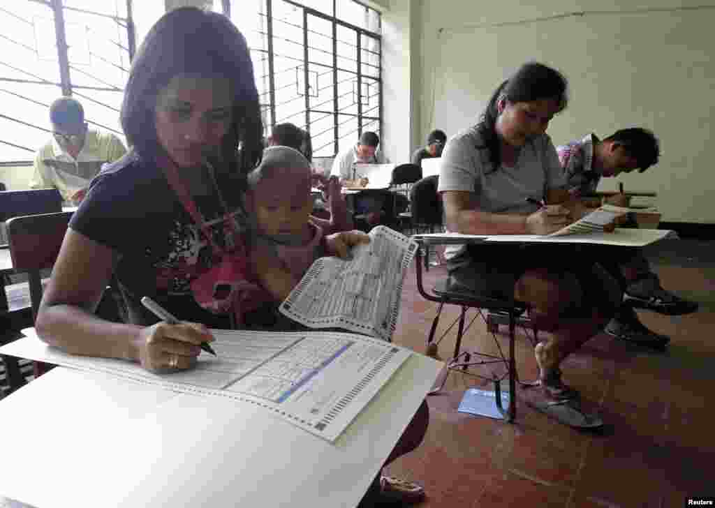 A mother with her daughter fills out a ballot form at a school in Manila, May 13, 2013.