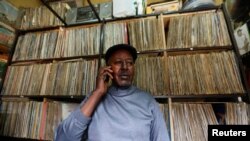 FILE - Vendor James Rugami talks to a customer on his cell phone inside his shop that specialize in selling second-hand vinyl records and vintage players at the Kenyatta Market in Nairobi, Nov. 24, 2016. 